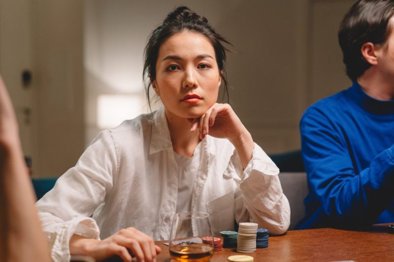 Focused young lady with unrecognizable friends playing board game with tokens in casino