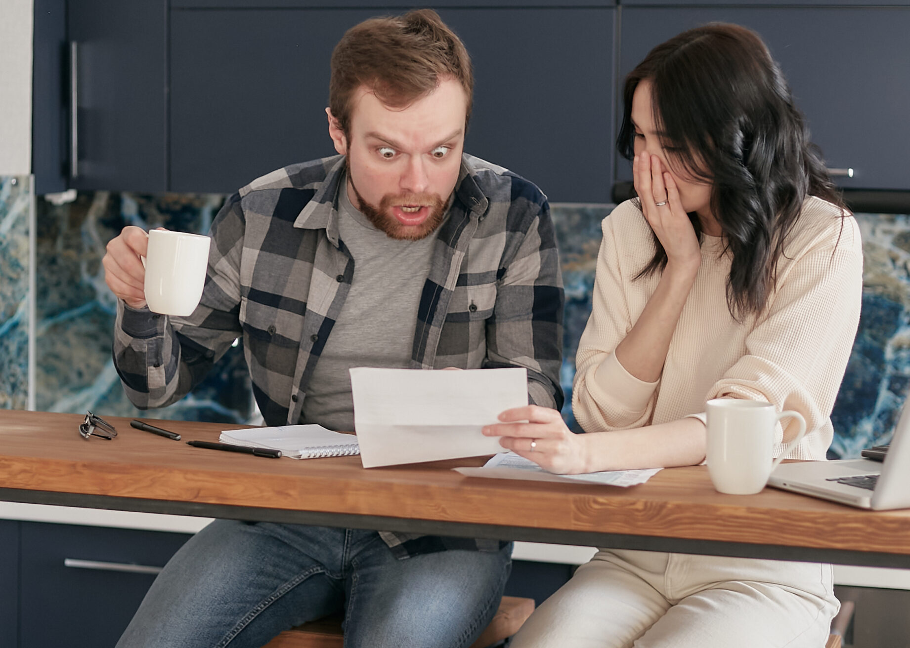 A couple sitting near the wooden table while looking at the document in shocked emotion