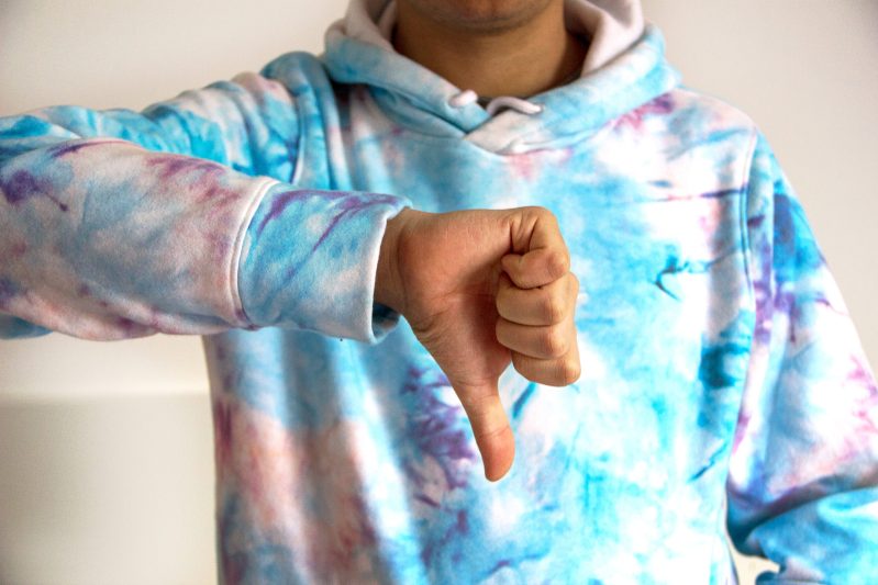A person in tie dye sweater doing thumbs down
