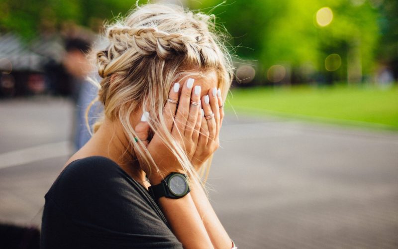 person covering face with hands outdoors